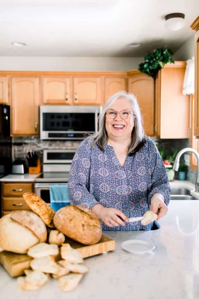 Glenda Embree standing next to freshly baked bread and buttering a slice of baguette.