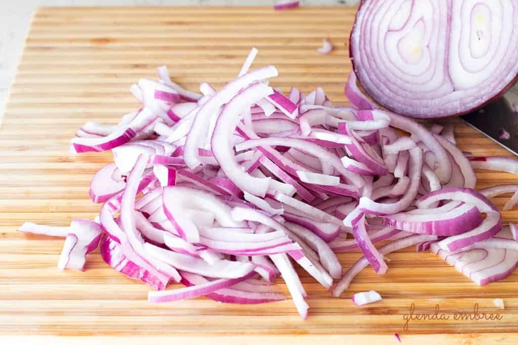 red onion sliced into thin strips on a cutting board