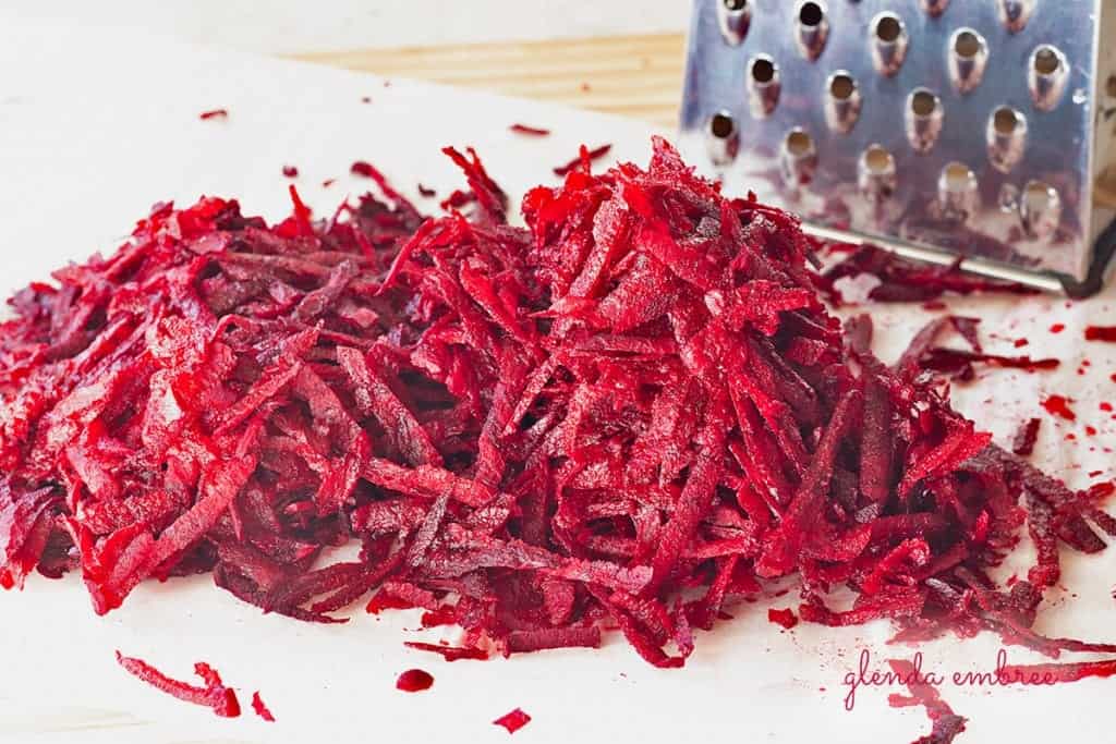 grated beet with box grater on a cutting board covered with parchment paper