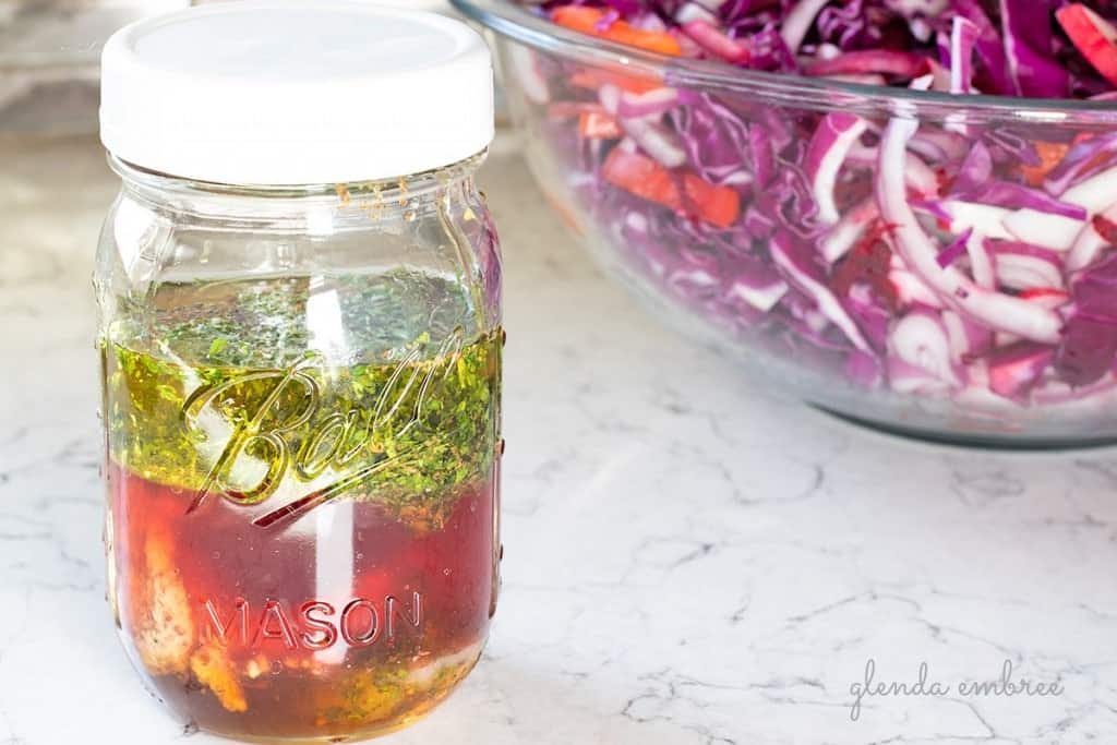 salad dressing ingredients in a mason jar: avocado oil, red wine vinegar, stone ground mustard, honey, parsley, celery seed, salt and pepper.