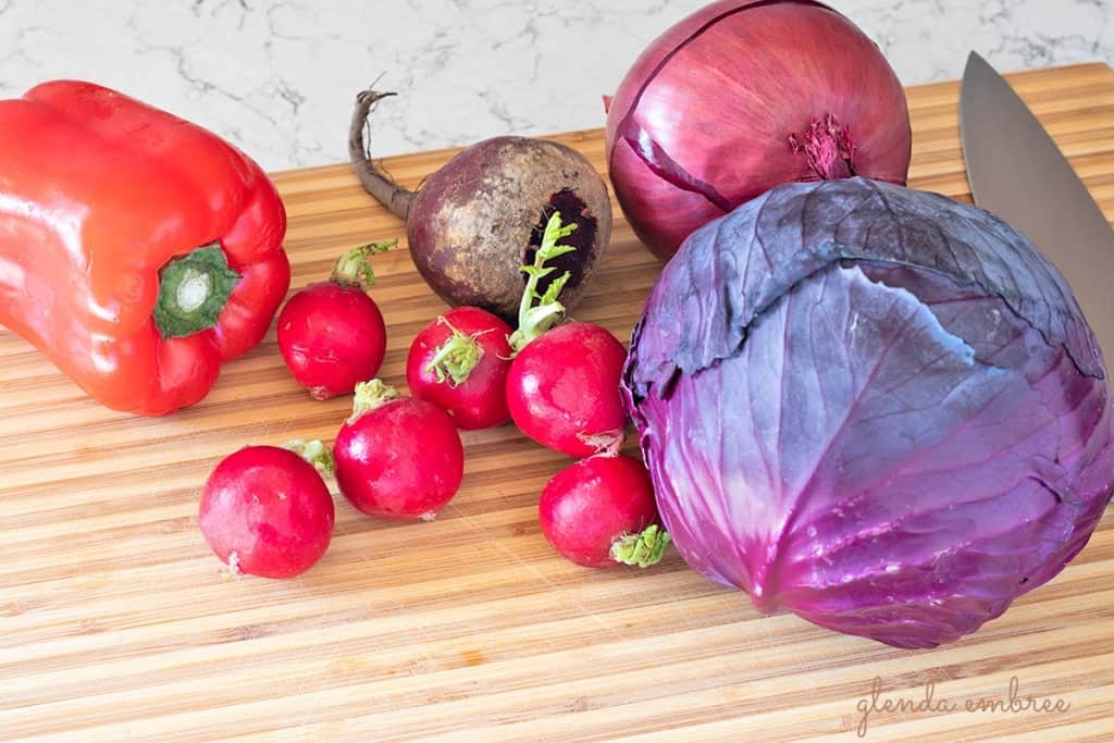 purple cabbage, red onion, radishes, beet and red bell pepper on a cutting board