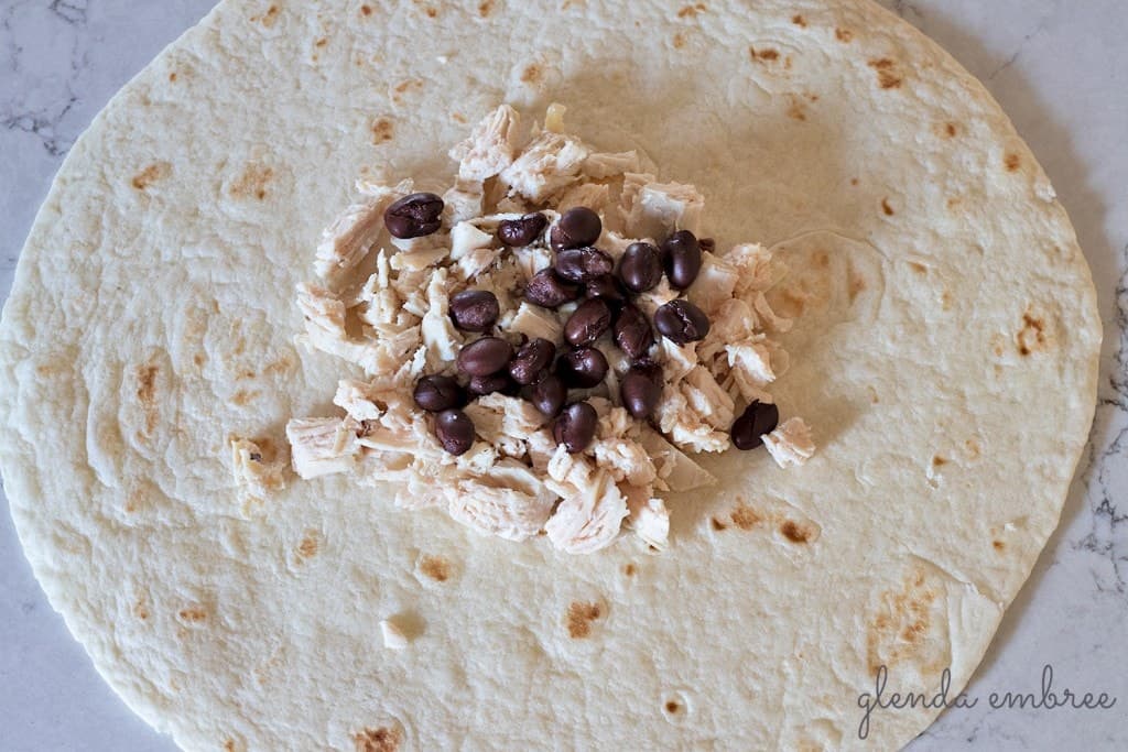 How to Assemble a Crunch Wrap: Add chicken and black beans to center of tortilla.
