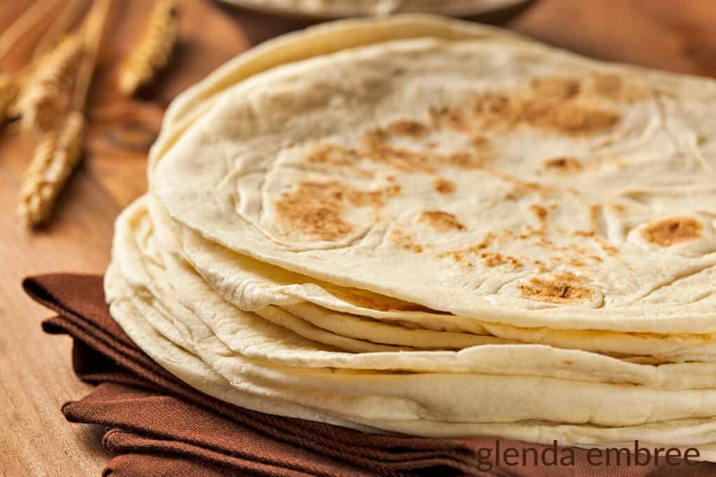 stack of flour tortillas on a folded brown kitchen towel