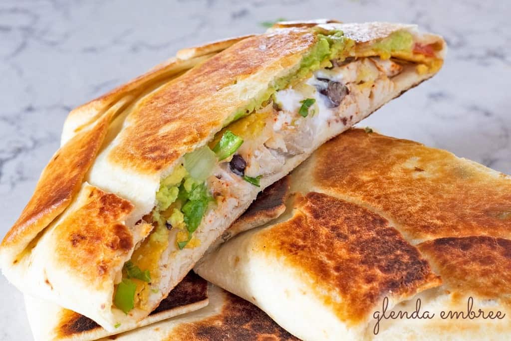 chicken crunch wrap supreme sliced and stacked on marble counter top