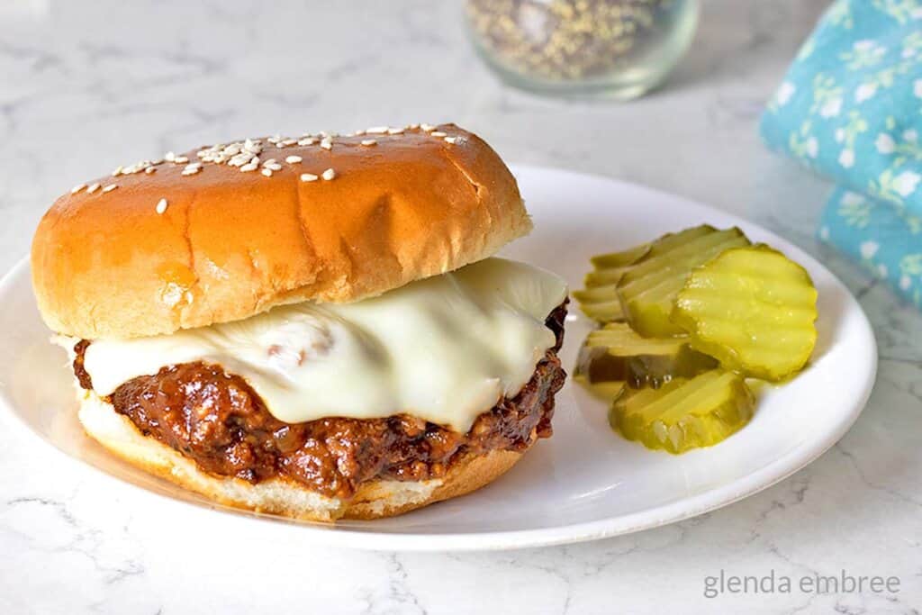 Easy Homemade Sloppy Joes on a white plate with cheese and pickles.
