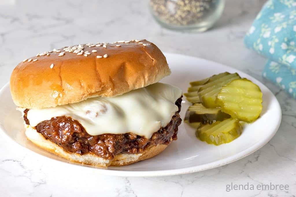 Best Sloppy Joes Recipe - sloppy joe sitting on a white plate with dill pickle chips