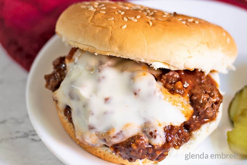 Best Sloppy Joes Recipe - sloppy joe sitting on a white plate with dill pickle chips