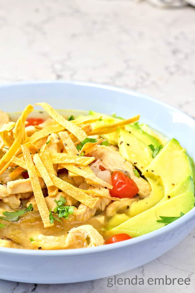 Avocado Lime Chicken Soup served in a pale blue stoneware bowl with avocado slices and crispy corn tortilla strips