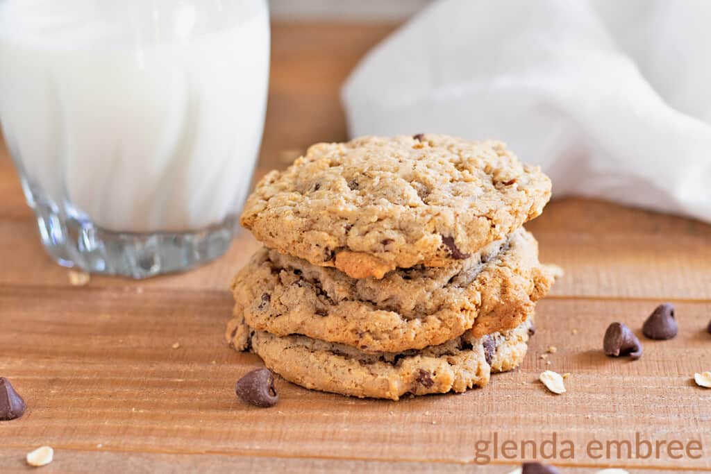 gluten free oatmeal chocolate chip cookies on a wooden table with a glas of milk and white napkin