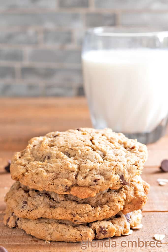 gluten free oatmeal chocolate chip cookies on a wooden table with a glas of milk and white napkin