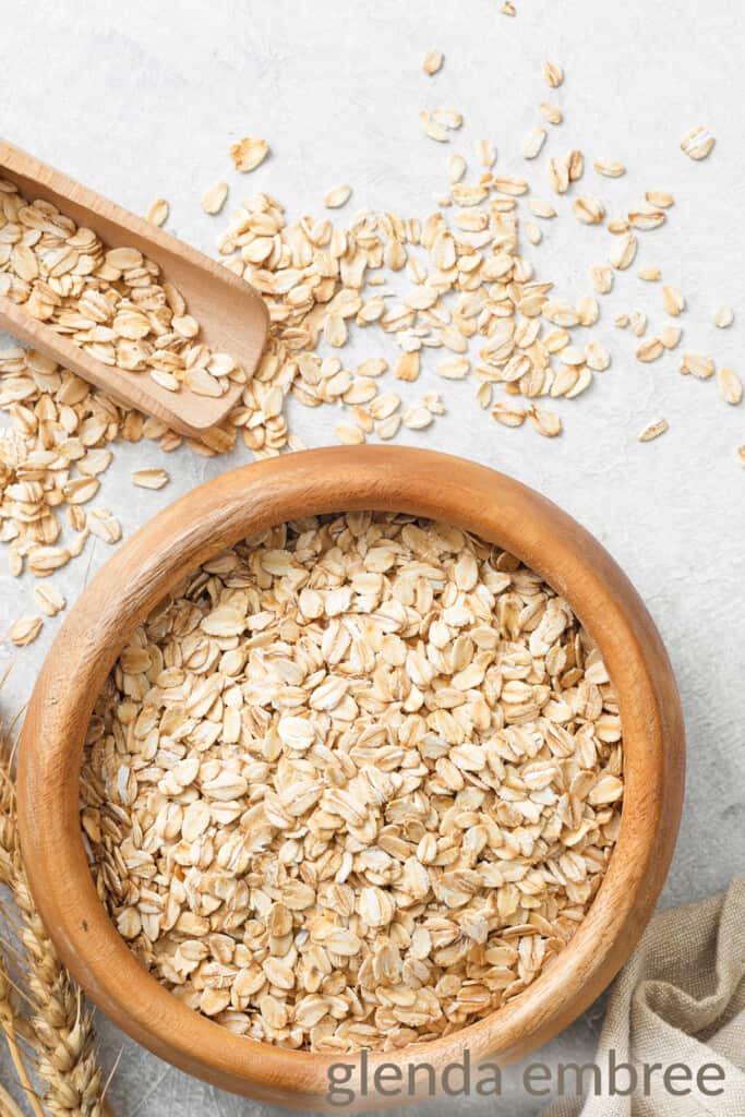 wooden bowl of raw rolled oats on a white counter with oats scattered about