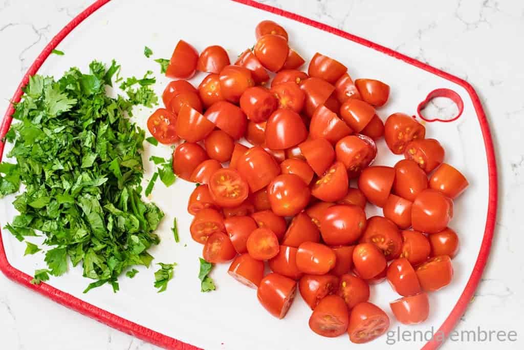 chopped cilantro and halved cherry tomatoes on a cutting board