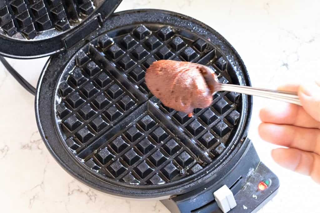 adding a spoonful of turtle cookie batter to a waffle iron