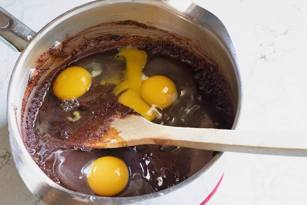 eggs added to chocolate batter in a sauce pan
