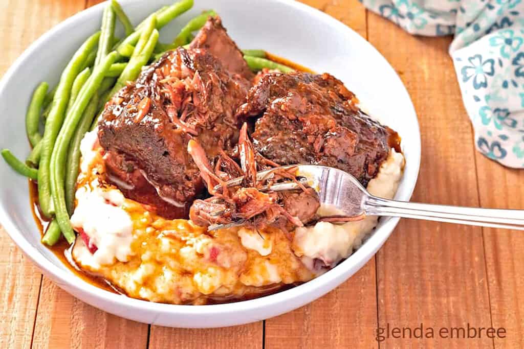 Braised Beef Short Ribs on a bed of garlic mashed potatoes with green beans on the side.