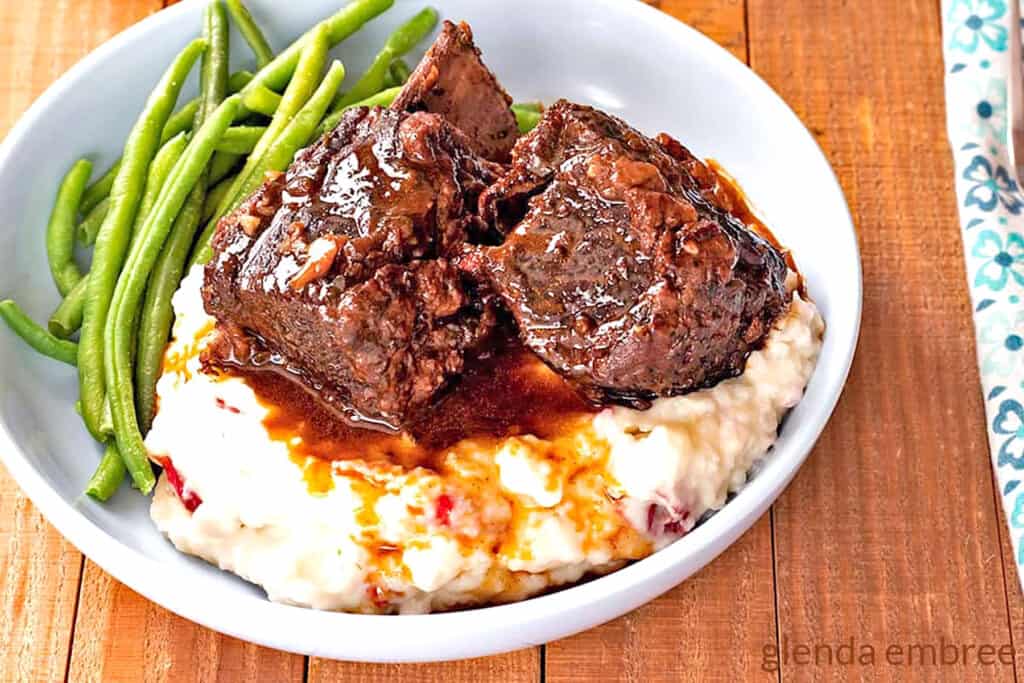 Braised Beef Short Ribs on a bed of garlic mashed potatoes with green beans on the side.