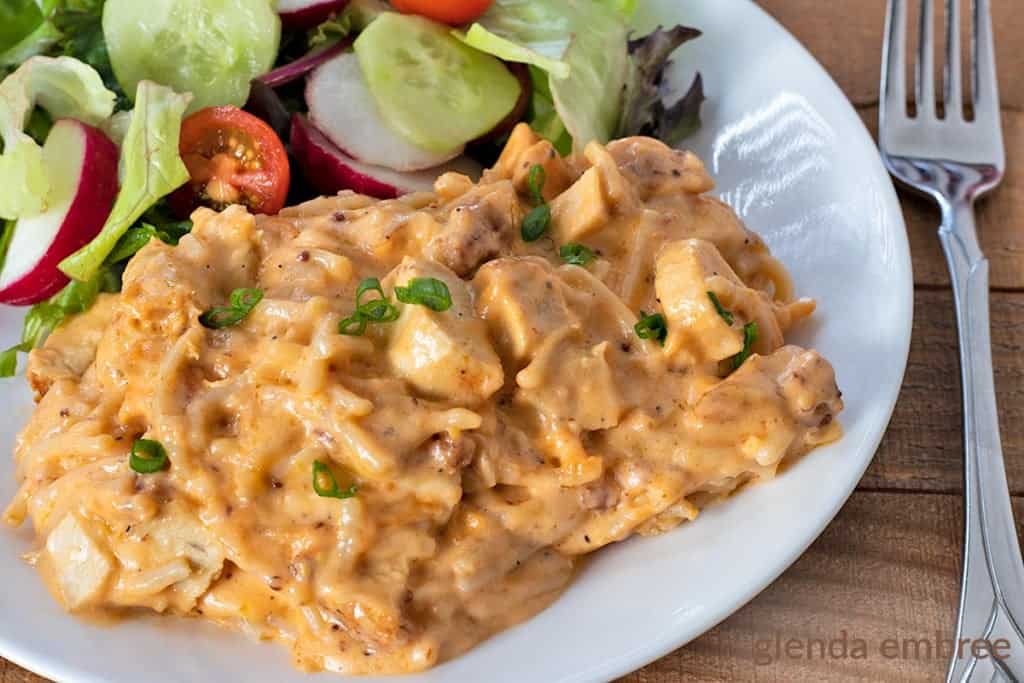 Cheesy Chicken Spaghetti served on a white plate with a green salad and veggies