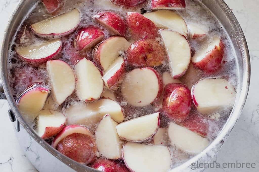 cut red potatoes covered with waterin a pot 