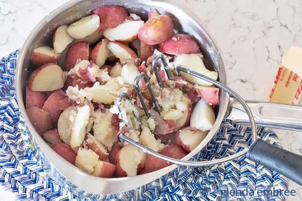 red potatoes in a pot  with potato masher