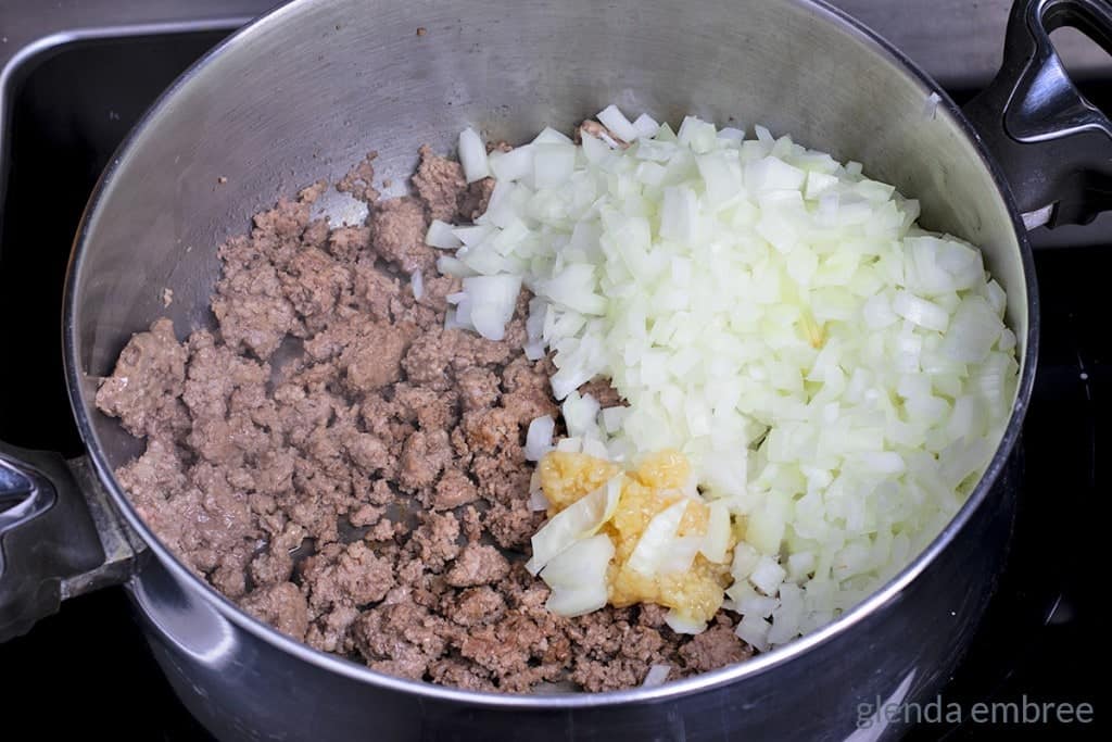 Adding onions and garlic to browned ground beef in a soup pot.