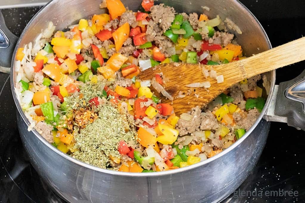 adding peppers and herbs to groundbeef and onions in a soup pot