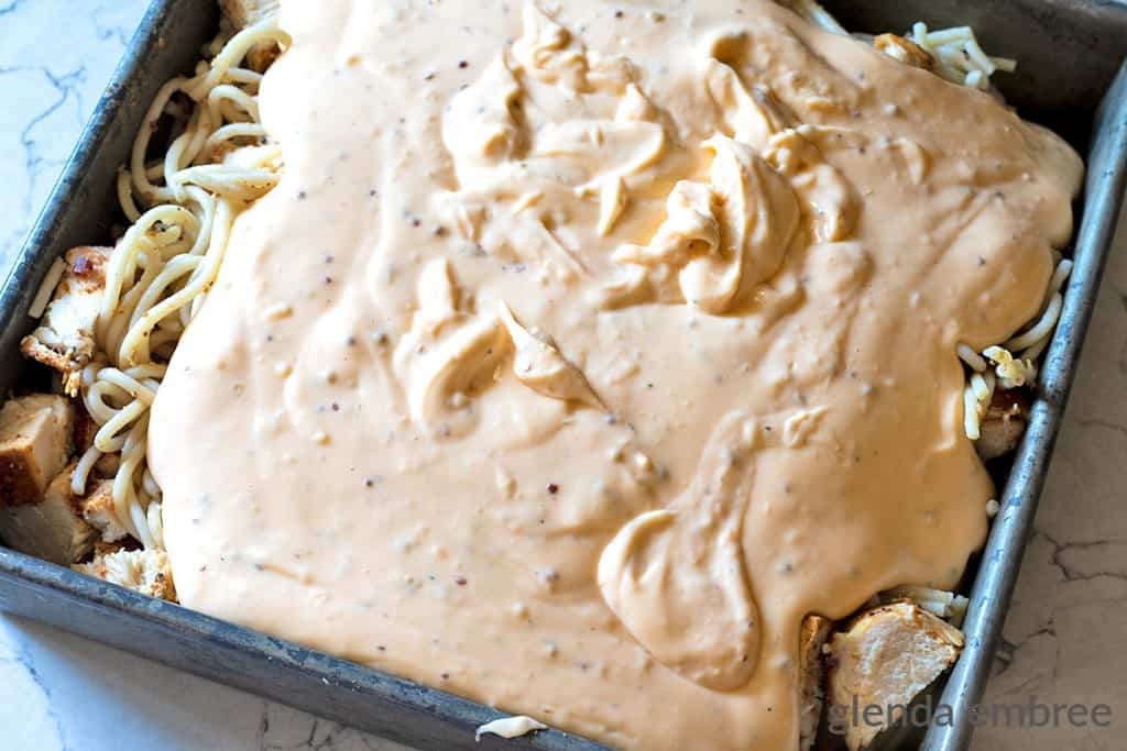 cheese sauce poured over chicken, bacon and spaghetti in 9x9 pan