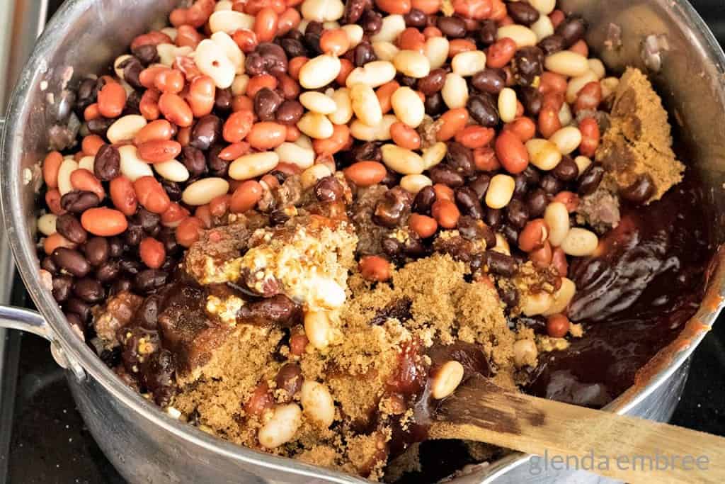 adding brown sugar and seasonings to baked beans