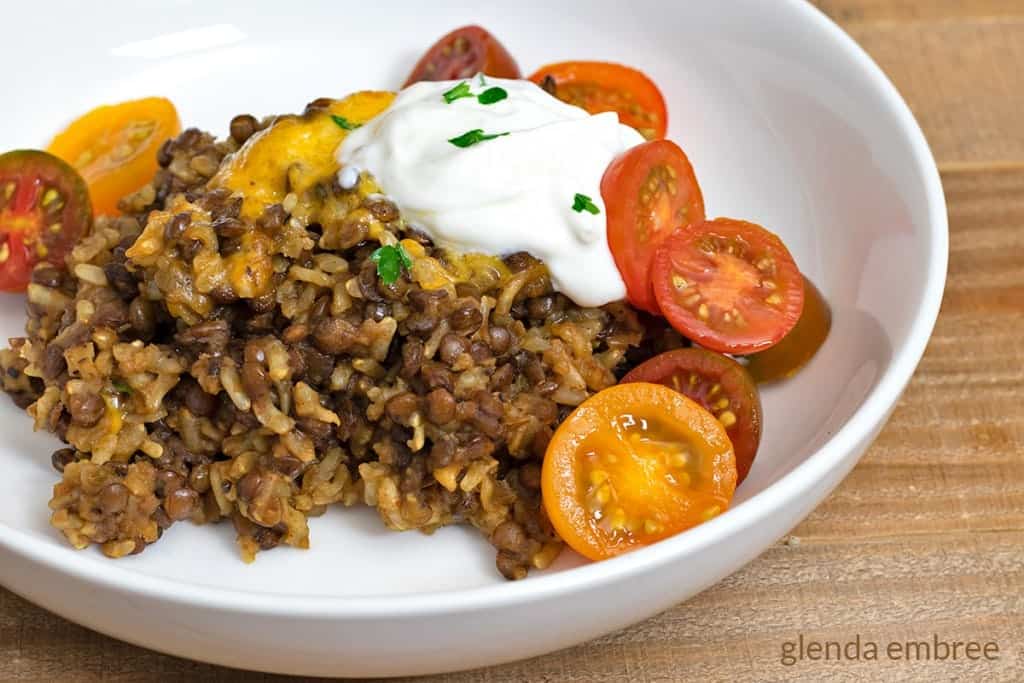Lentils and Rice Casserole in white bowl and garnished with sour cream, sliced cherry tomatoes and minced parsley