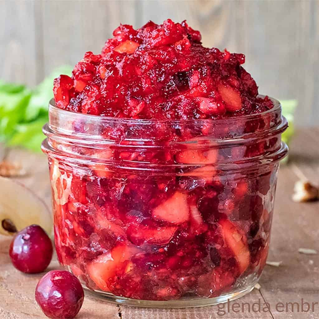 Cranberry Apple Salad in a small mason jar on a wooden table with cranberries, apple slices and pecans strewn around