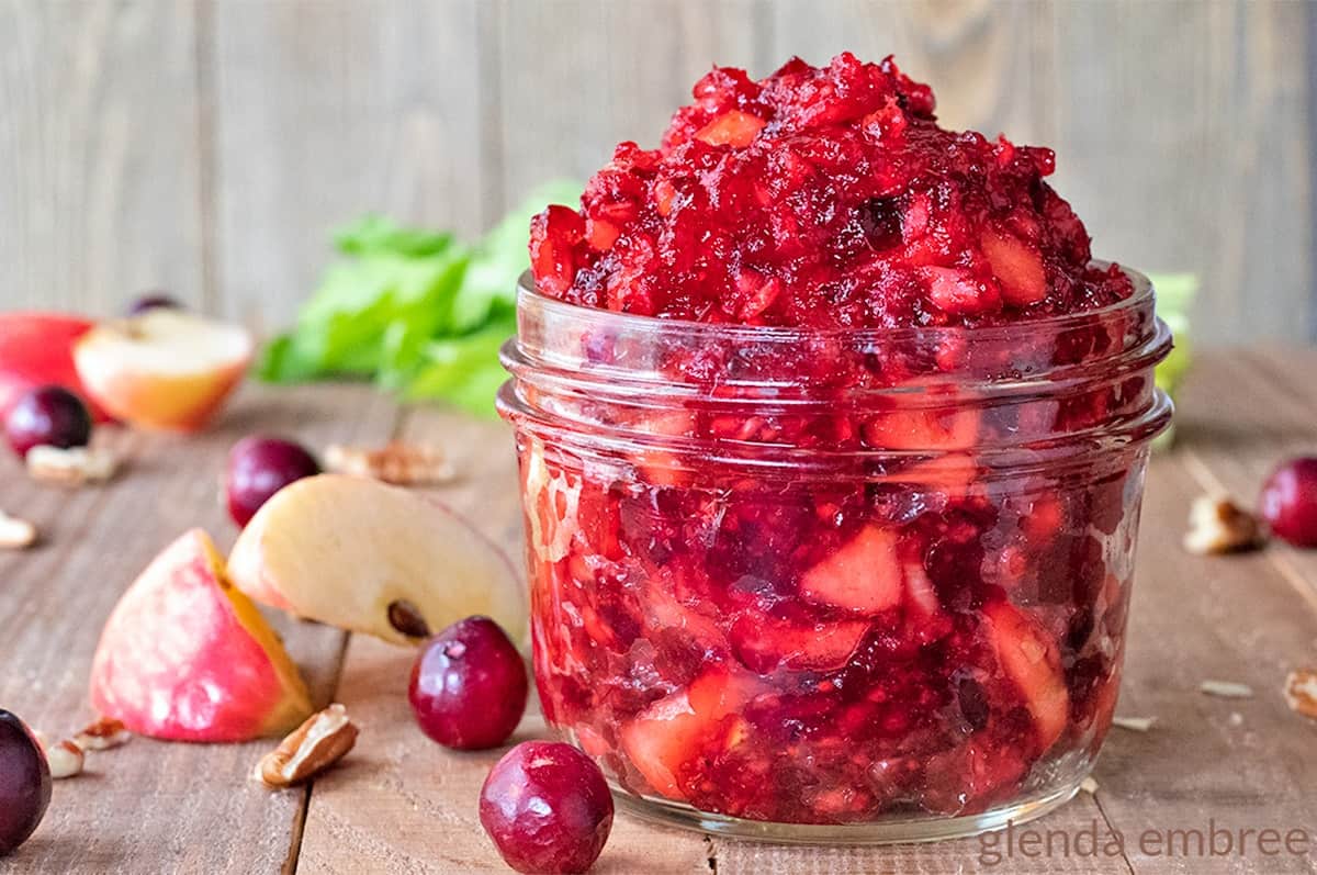 Cranberry Apple Salad in a small mason jar on a wooden table with cranberries, apple slices and pecans strewn around