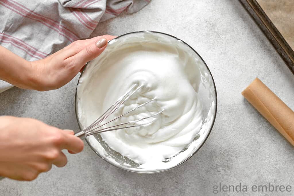 hands holding a whisk and whipping homemade whipped cream in a bowl