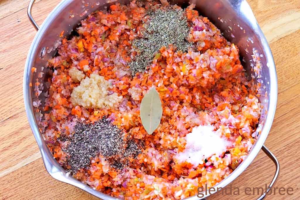 ground vegetables (carrots, onions, peppers), a bay leaf and other seasonings in a stew pot