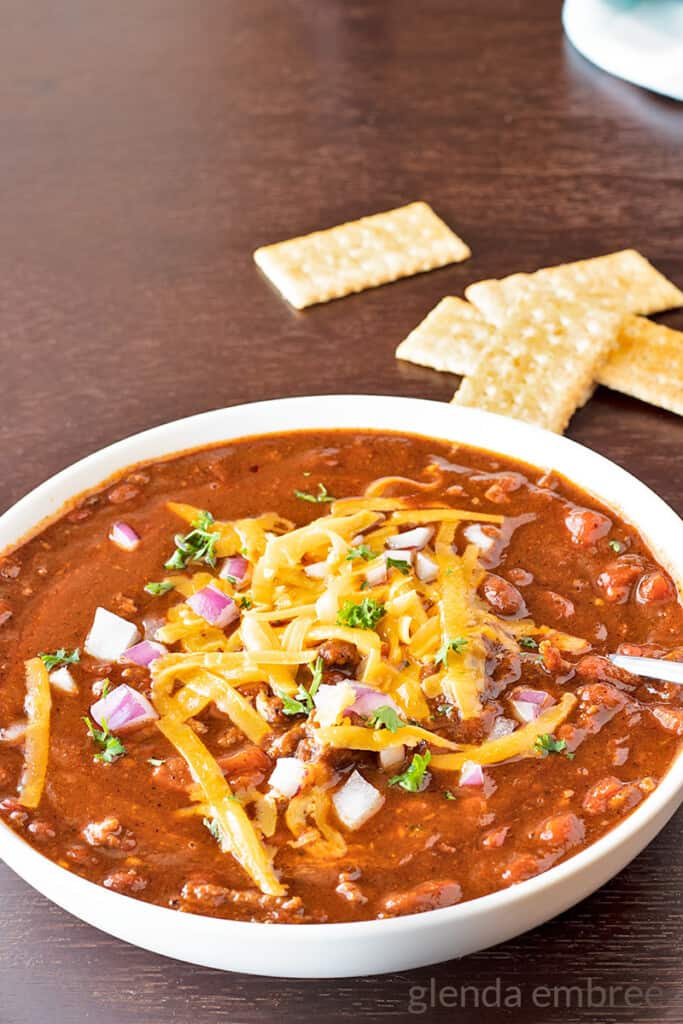 best easy chili recipe - chili in an ivory stoneware bowl topped with grated cheddar, onions and cilantro