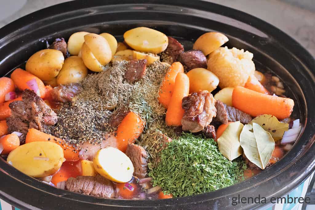 herbs added to slow cooker with beef, potatoes, carrots and onions