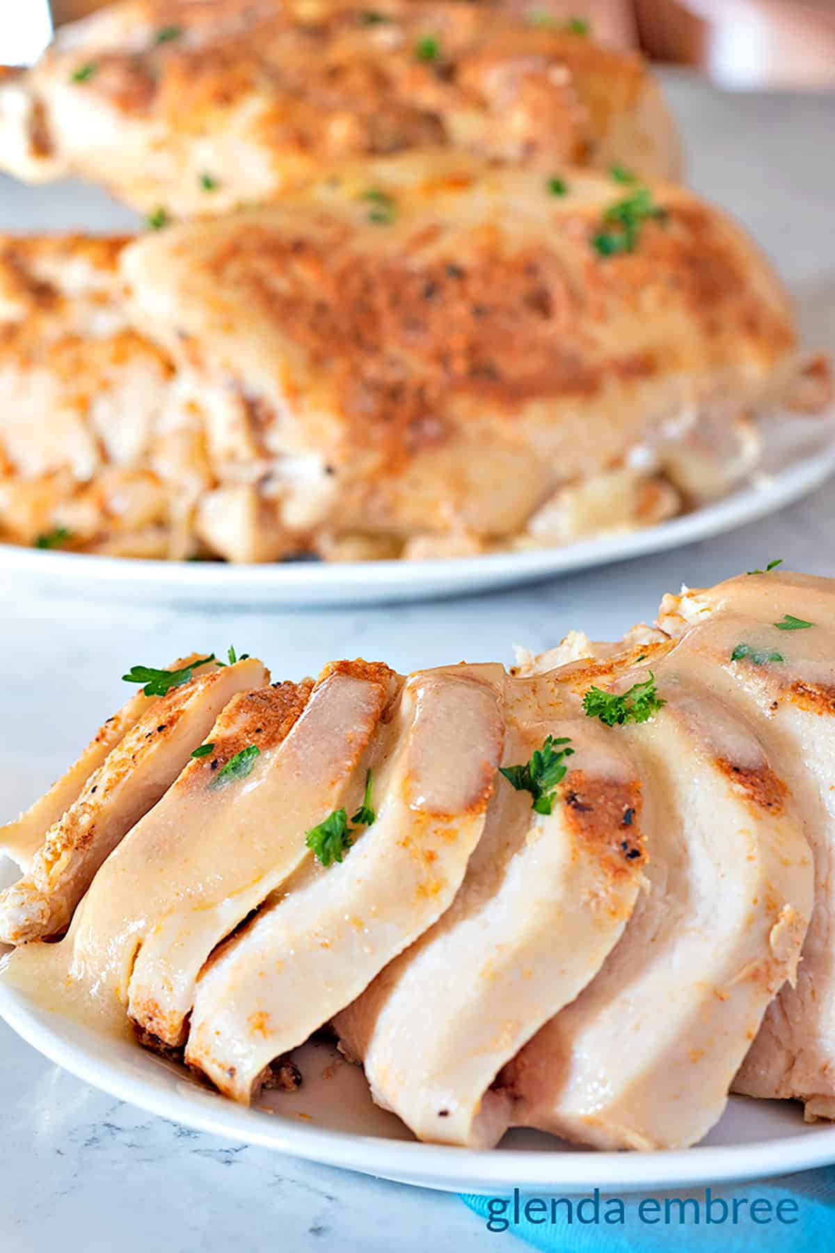 Slow Cooker Chicken Breasts sliced on a plate with a platter of slow cooker chicken breasts in the background