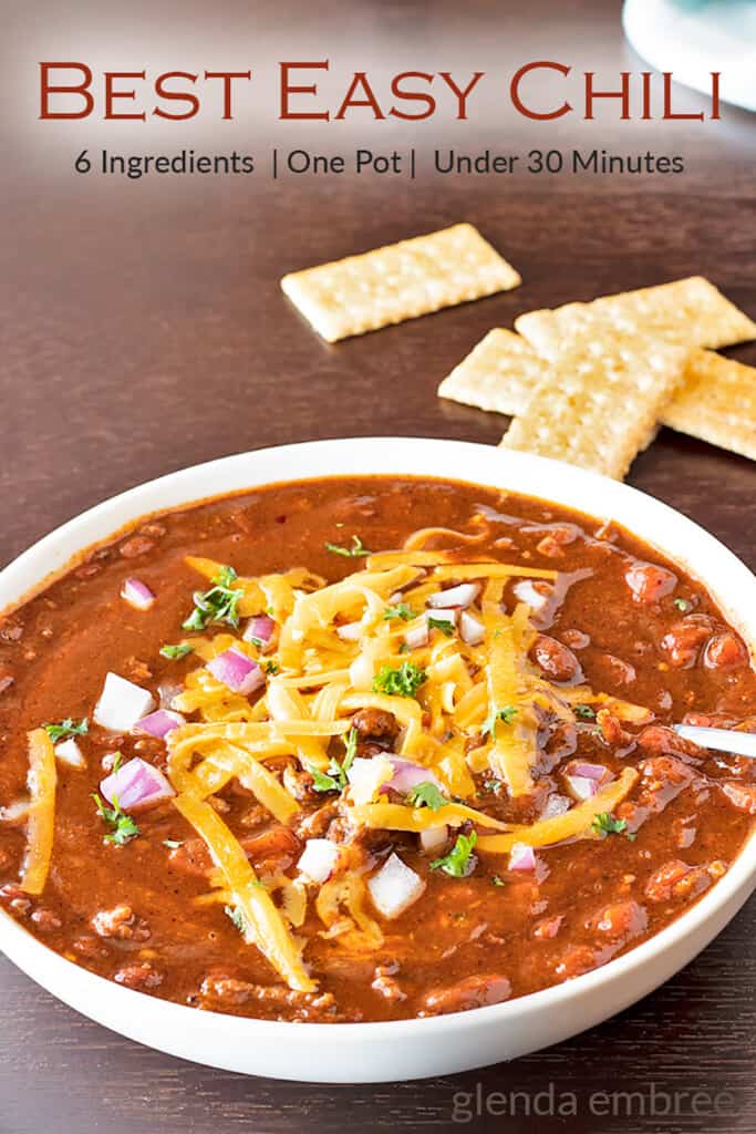 best easy chili in a white bowl topped with grated cheddar, minced red onion and cilantro