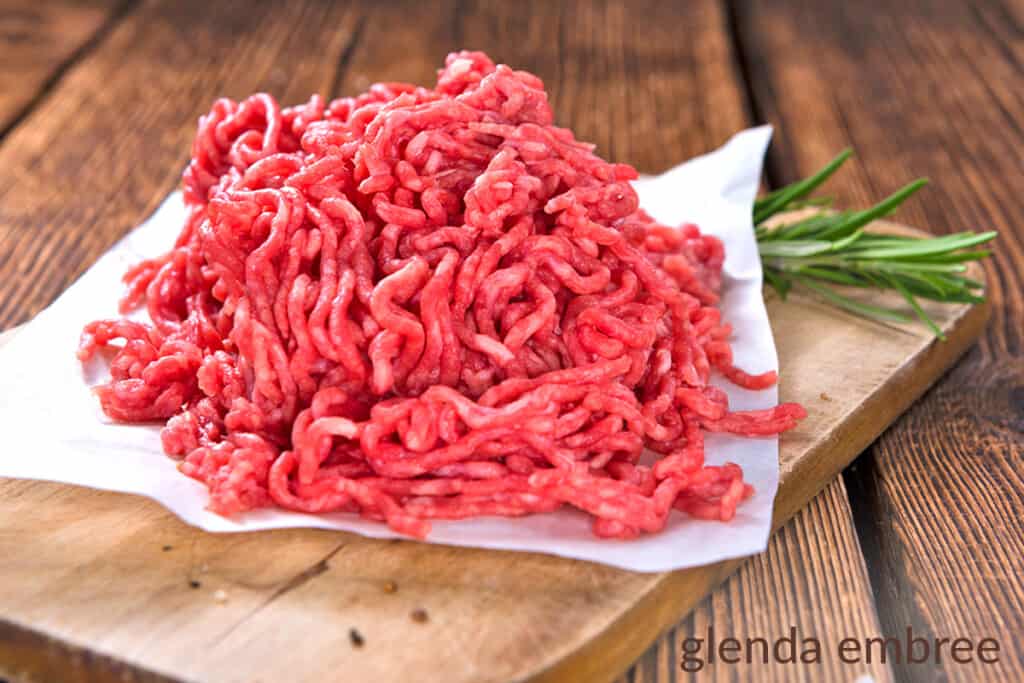 raw ground beef on parchment paper sitting on a wooden cutting board