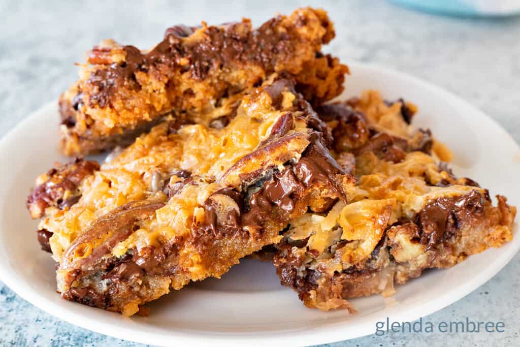 magic cookie bars on a white plate with a blue print napkin in the background