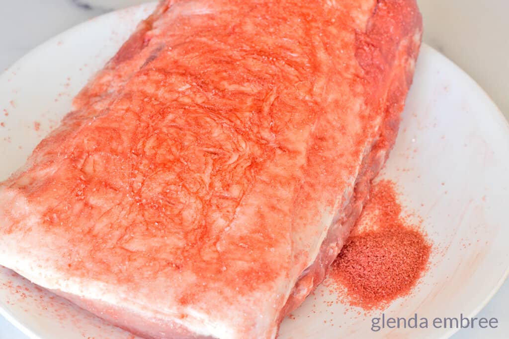 raw pork loin being seasoned with red Hawaiian sea salt
