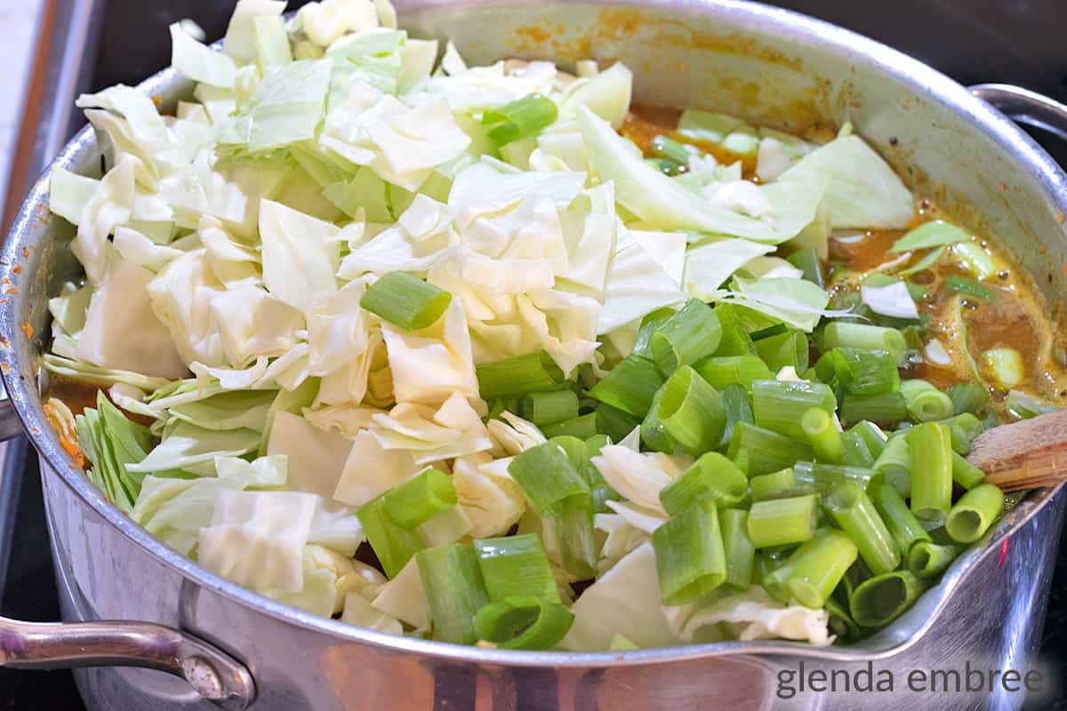 adding white cabbage and green onions to a stainless steel soup pot