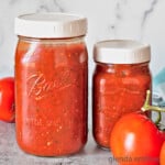 homemade marinara recipe in jars on concrete counter top with fresh tomatoes and a blue and white gingham napkin