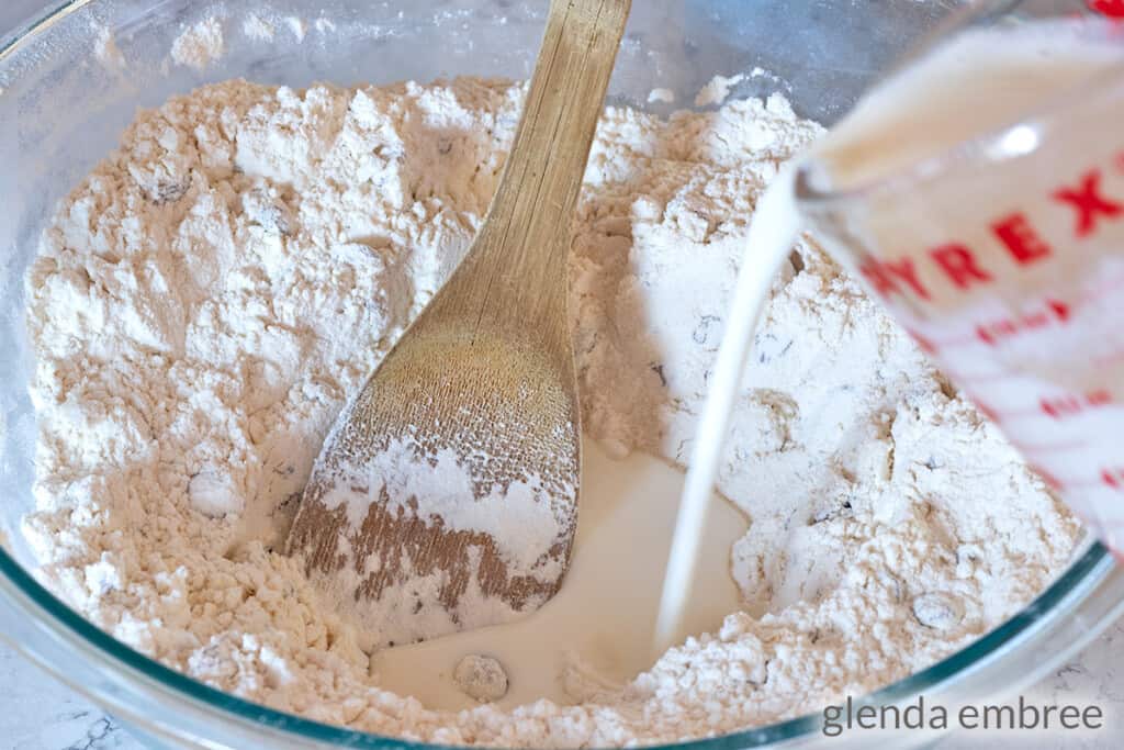 adding buttermilk to dry ingredients in a clear glass mixing bowl
