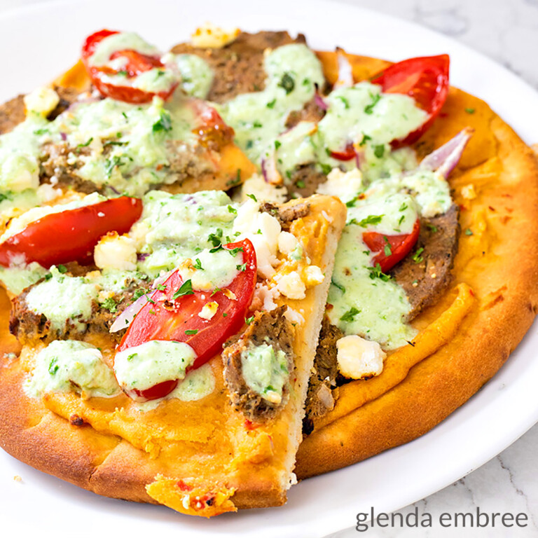 gyro pizza made on a pita flat bread with roasted red pepper hummus, homemade gyro meat, cherry tomatoes, slivered red onion, feta cheese, tzatziki sauce and a sprinkling of parsely