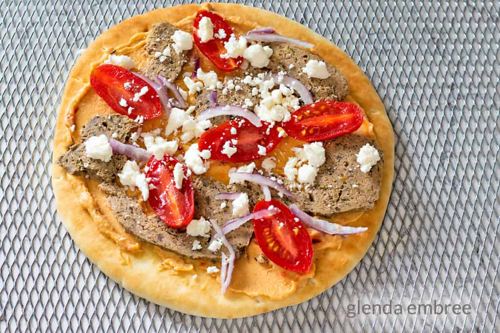 prebaked gyro pizza made on a pita flat bread with roasted red pepper hummus, homemade gyro meat, cherry tomatoes, slivered red onion and feta cheese