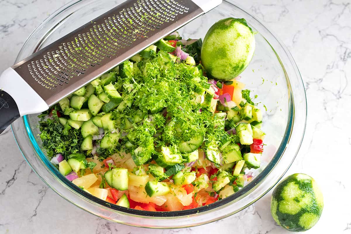 pineapple salsa ingredients in a glass mixing bowl with a microplane and lime zest