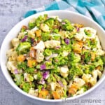 easy broccoli cauliflower salad recipe - salad in a round, white ceramic bowl ona concrete counter with a turquoise and white checked napkin