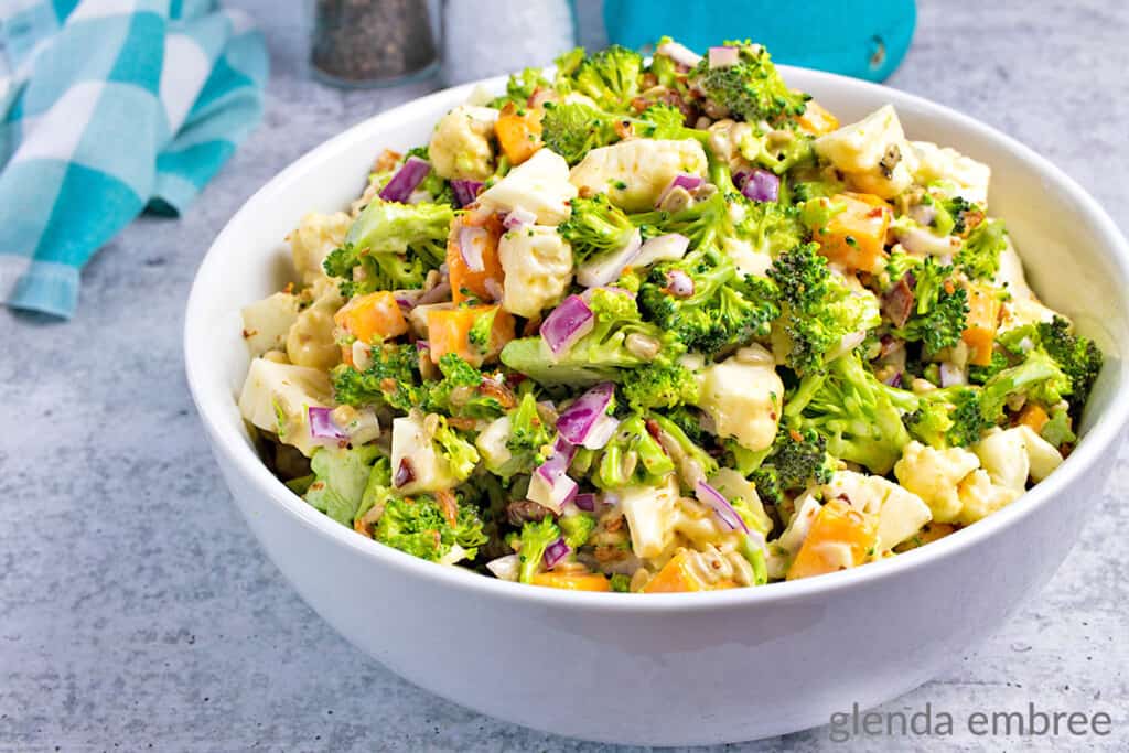 easy broccoli cauliflower salad recipe - salad in a round, white ceramic bowl ona concrete counter with a turquoise and white checked napkin