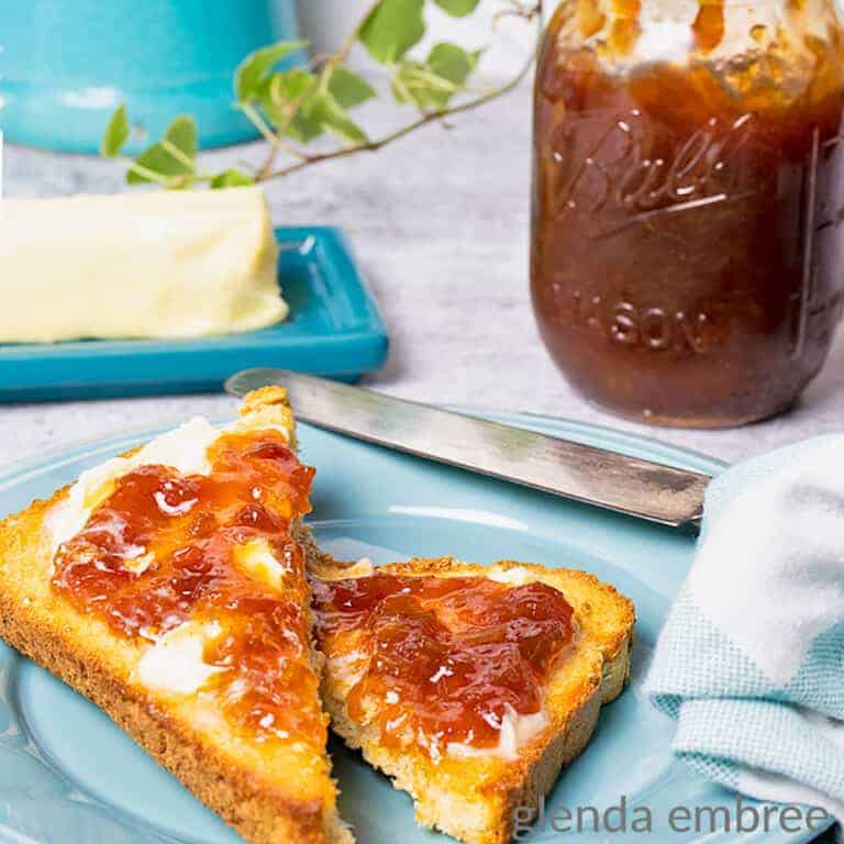 rhubarb jam in a pint jar near a blue pate with toast that is spread with butter and rhubarb jam