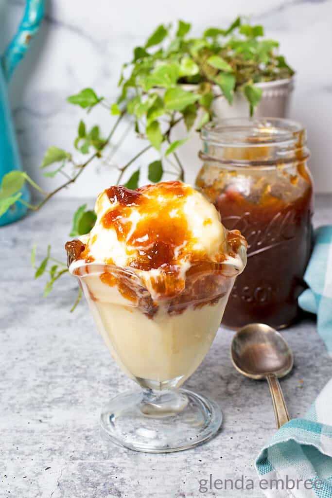 rhubarb jam in a pint jar behind an ice cream sundae of vanilla ice cream drizzled with rhubarb jam