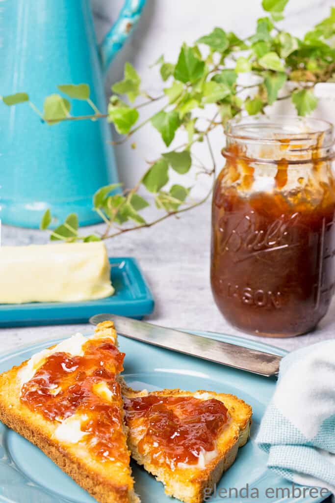 rhubarb jam in a pint jar near a blue pate with toast that is spread with butter and rhubarb jam